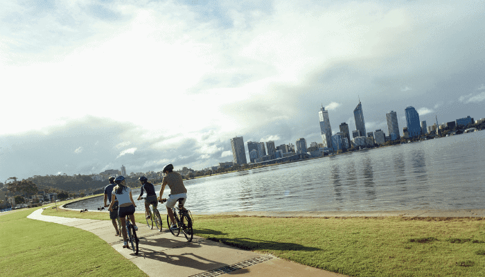 a group of people riding bikes on a path by a body of water