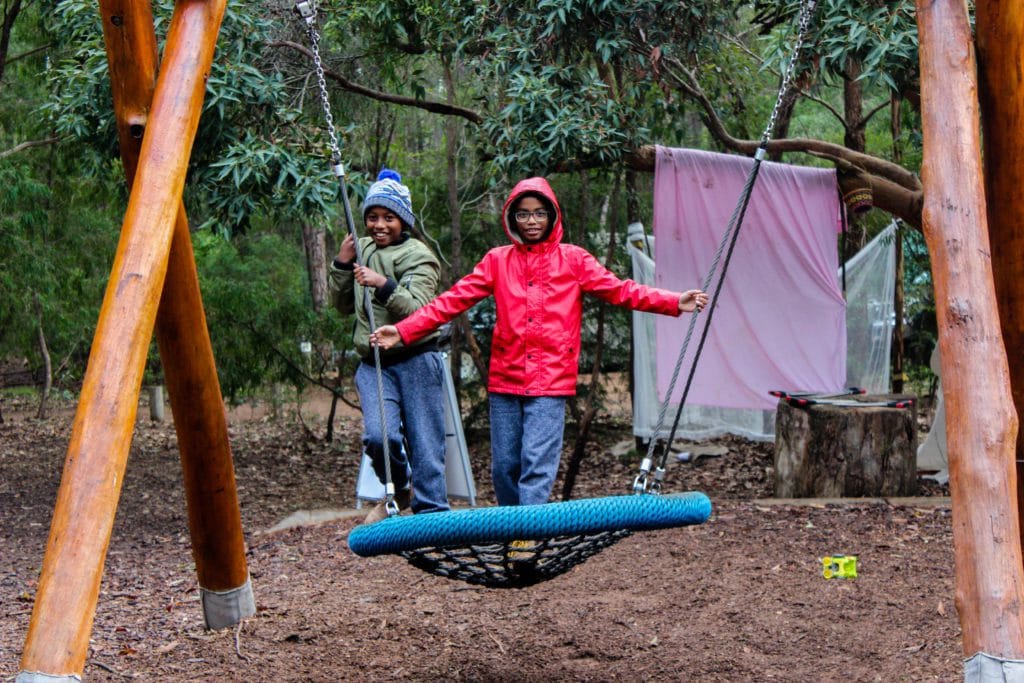 a couple of kids playing on a swing set in the woods
