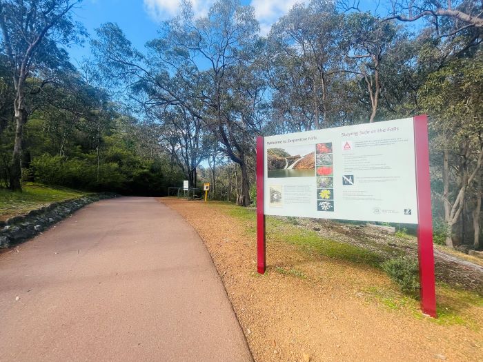 A photo of a sign beside a path at Serpentine National Park, surrounded by tall trees.