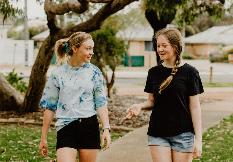 A photo of two girls walking and talking through a local park.