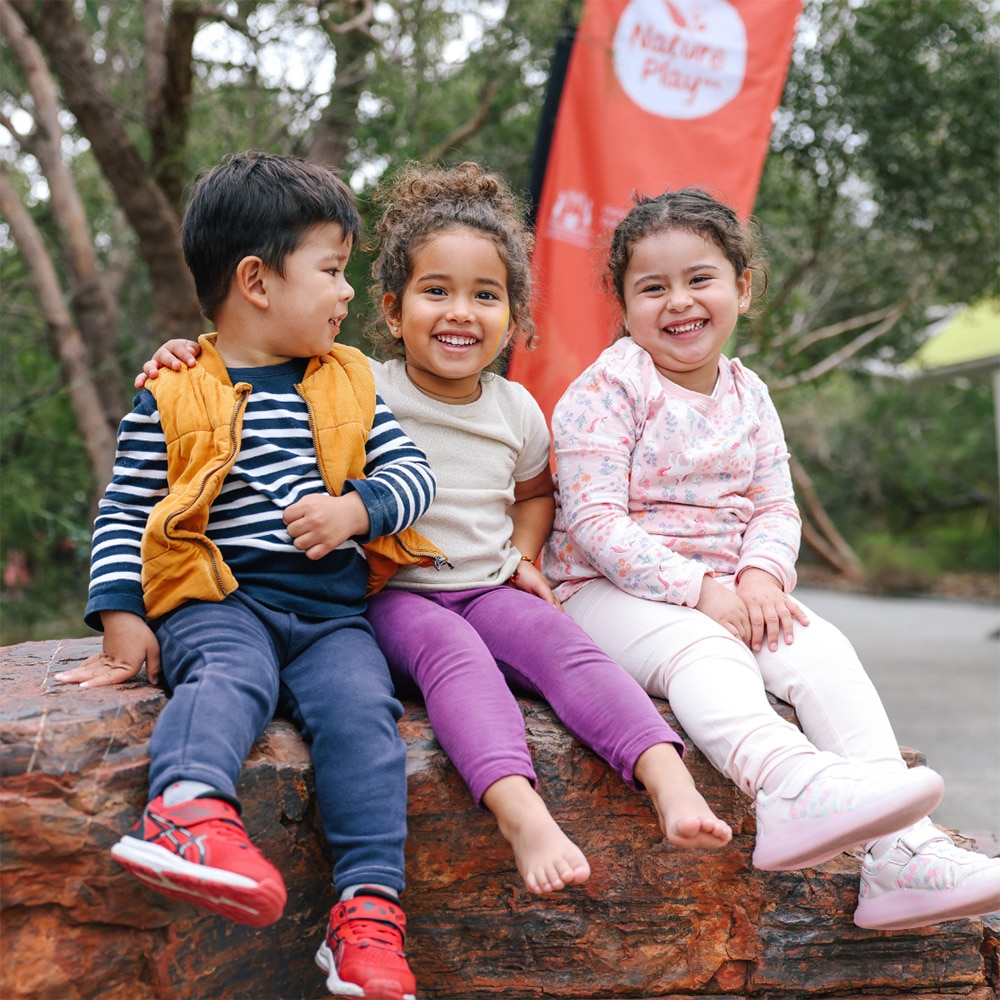 A photo of three children sitting on a rock in nature, smiling and laughing.