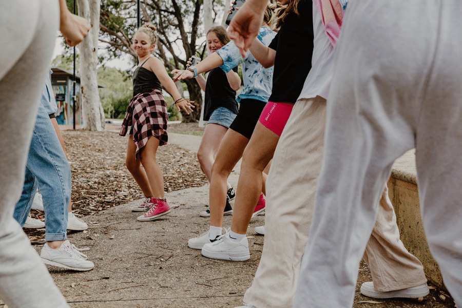 A group of happy tween and teen girls dance at a local park.